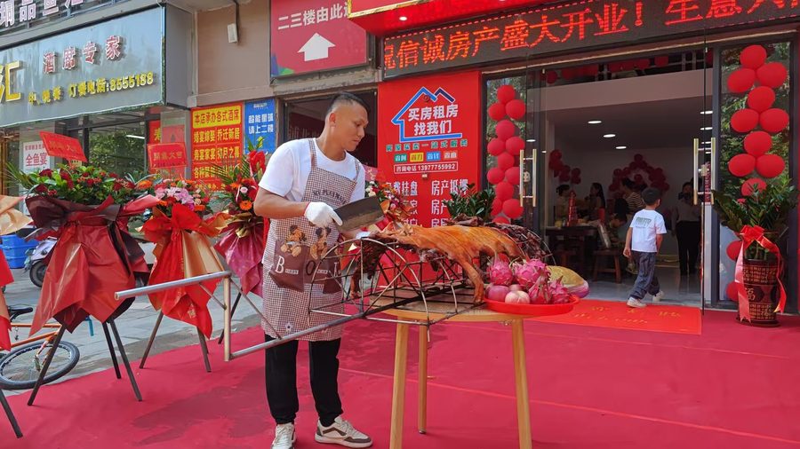 浦北信诚房产奥园广场直营店开业当天的现场烤全猪答谢活动，门店入口与花篮